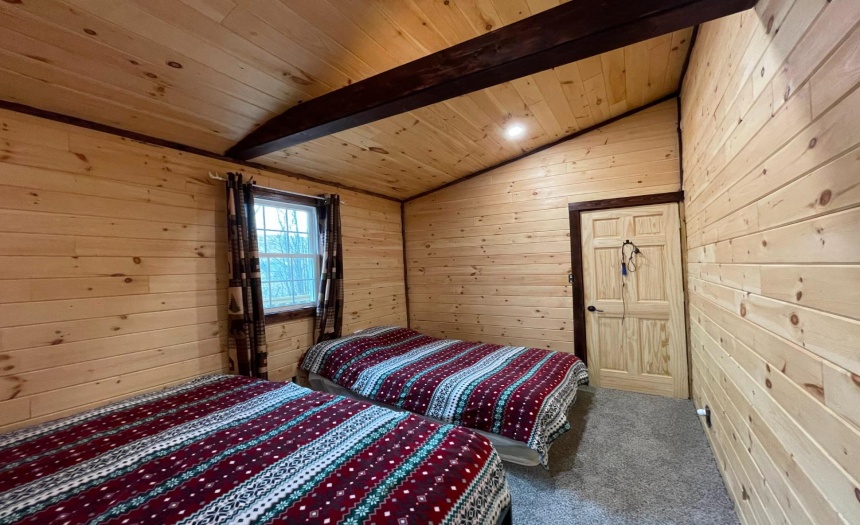 Large bedroom with carpet, open beam ceiling design & log walls
