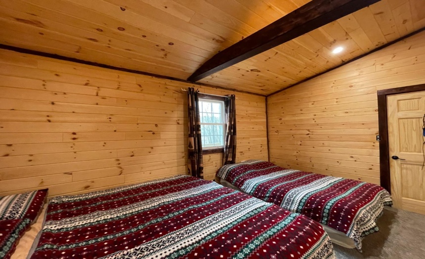Large bedroom with carpet, open beam ceiling design & log walls