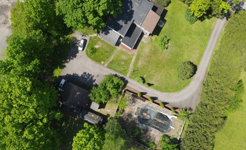 Topside view of the pool, bath house, garage, paved drive, parking area and home.